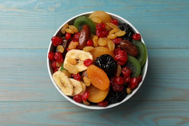 Photo of Mix of different dried fruits in bowl on light blue wooden table, top view