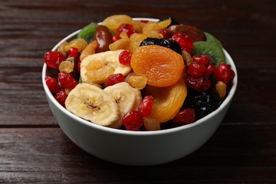 Photo of Mix of different dried fruits in bowl on wooden table, closeup