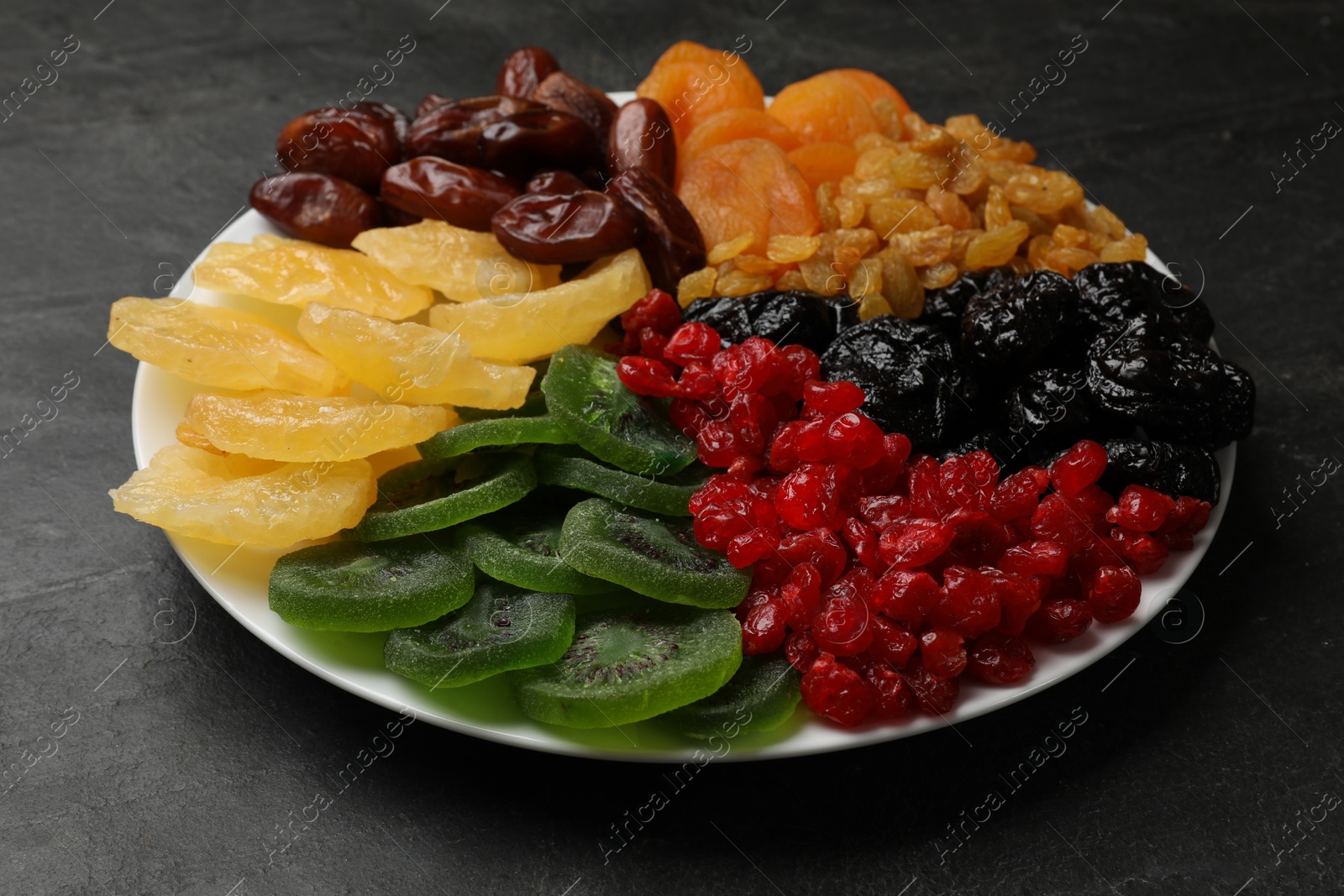 Photo of Mix of different dried fruits on black textured table, closeup