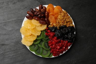 Photo of Mix of different dried fruits on black textured table, top view