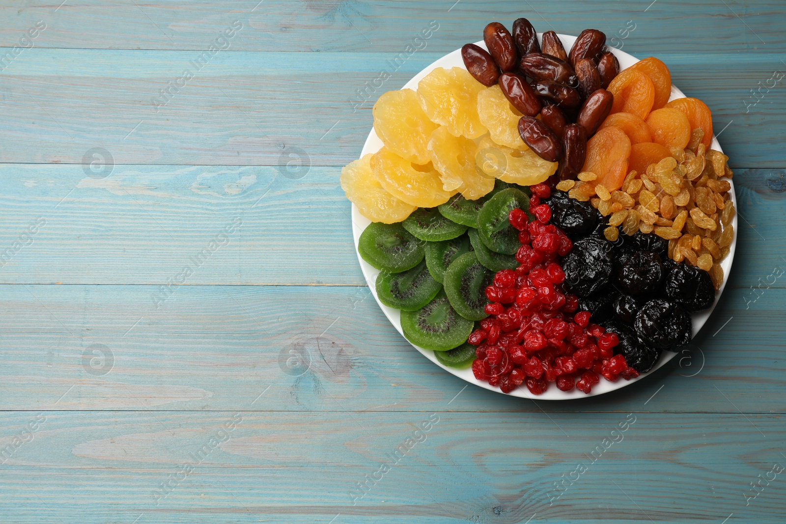 Photo of Mix of different dried fruits on light blue wooden table, top view. Space for text