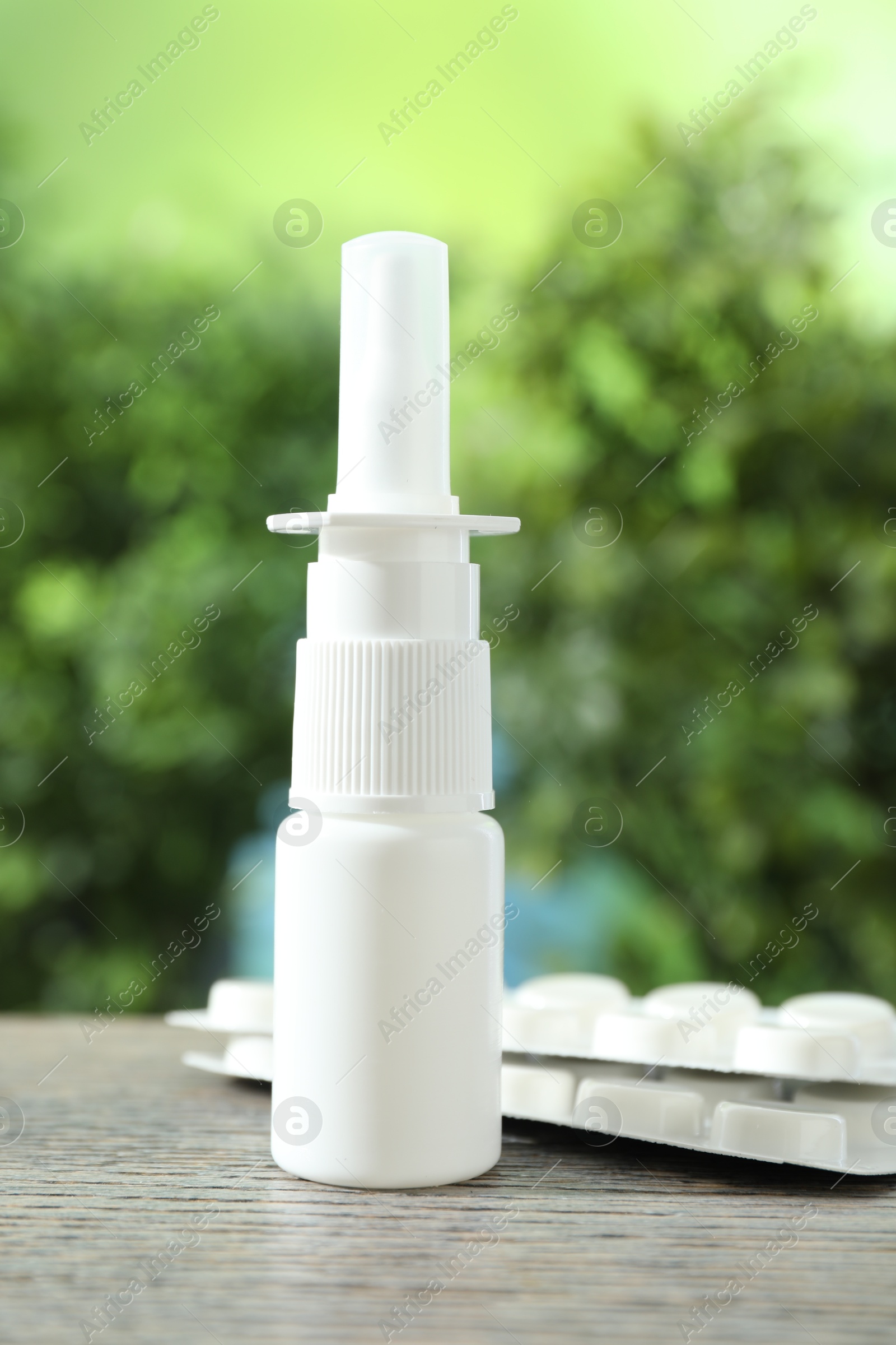 Photo of Allergy treatment. Nasal spray and pills on wooden table against blurred background