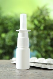 Photo of Allergy treatment. Nasal spray and pills on wooden table against blurred background