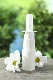 Photo of Allergy treatment. Nasal spray and flowers on wooden table against blurred background