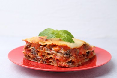 Photo of Piece of delicious cooked lasagna with basil on light table, closeup