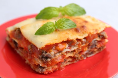 Photo of Piece of delicious cooked lasagna with basil on plate, closeup