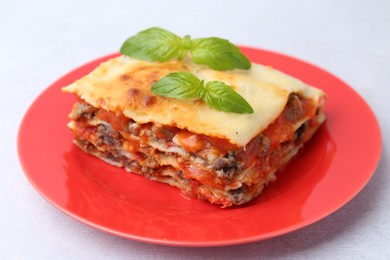 Photo of Piece of delicious cooked lasagna with basil on light table, closeup