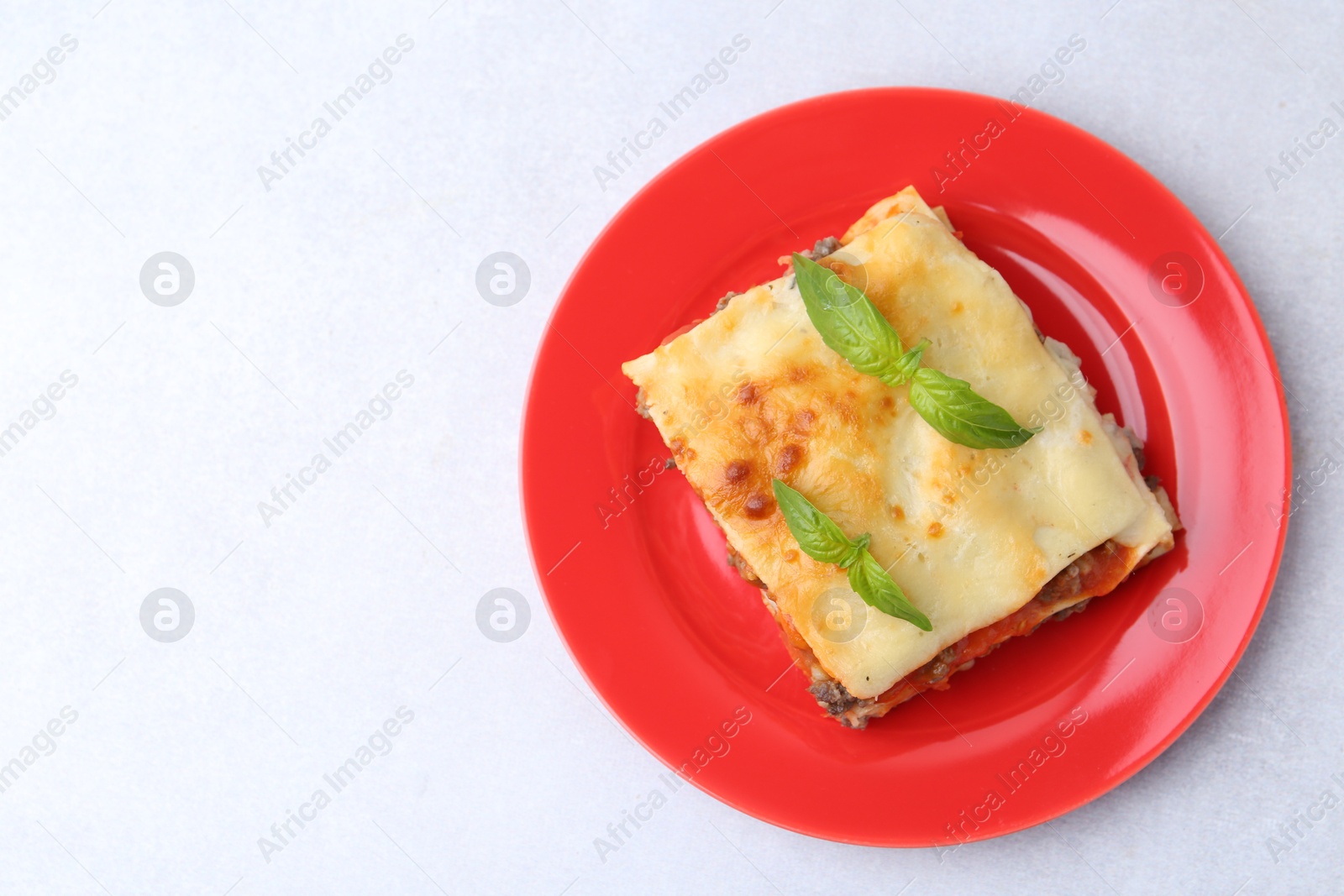 Photo of Piece of delicious cooked lasagna with basil on light table, top view. Space for text