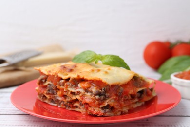 Photo of Piece of delicious cooked lasagna with basil on light wooden table, closeup