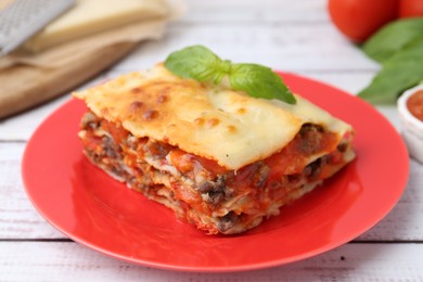 Photo of Piece of delicious cooked lasagna with basil on light wooden table, closeup