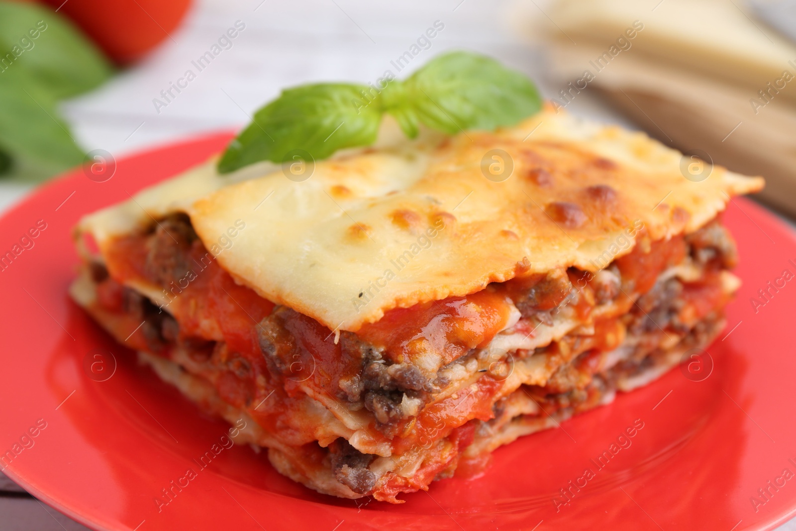 Photo of Piece of delicious cooked lasagna with basil on table, closeup