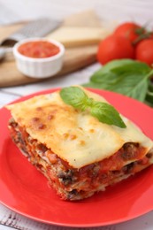 Photo of Piece of delicious cooked lasagna with basil on table, closeup