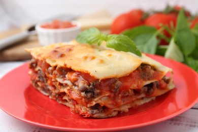 Photo of Piece of delicious cooked lasagna with basil on table, closeup