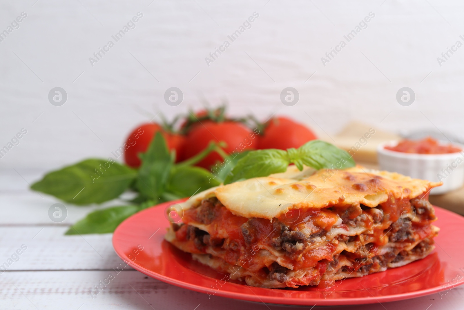 Photo of Piece of delicious cooked lasagna with basil on light wooden table, closeup