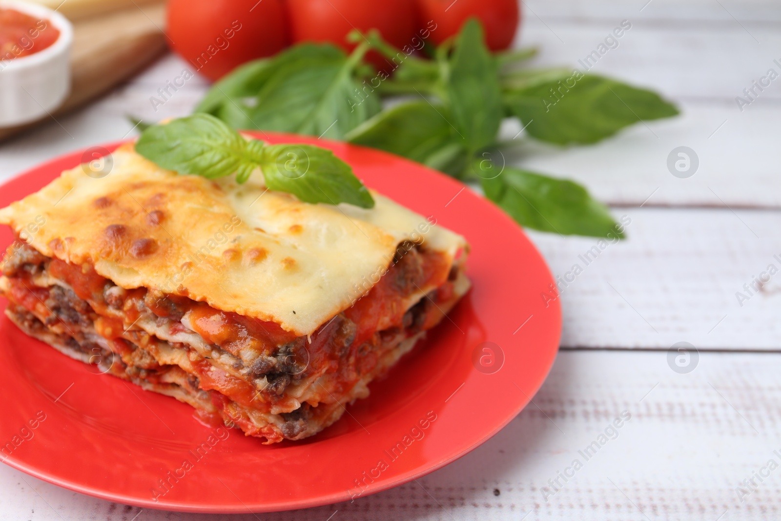 Photo of Piece of delicious cooked lasagna with basil on light wooden table, closeup. Space for text