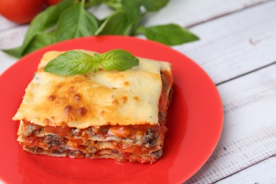 Photo of Piece of delicious cooked lasagna with basil on light wooden table, closeup