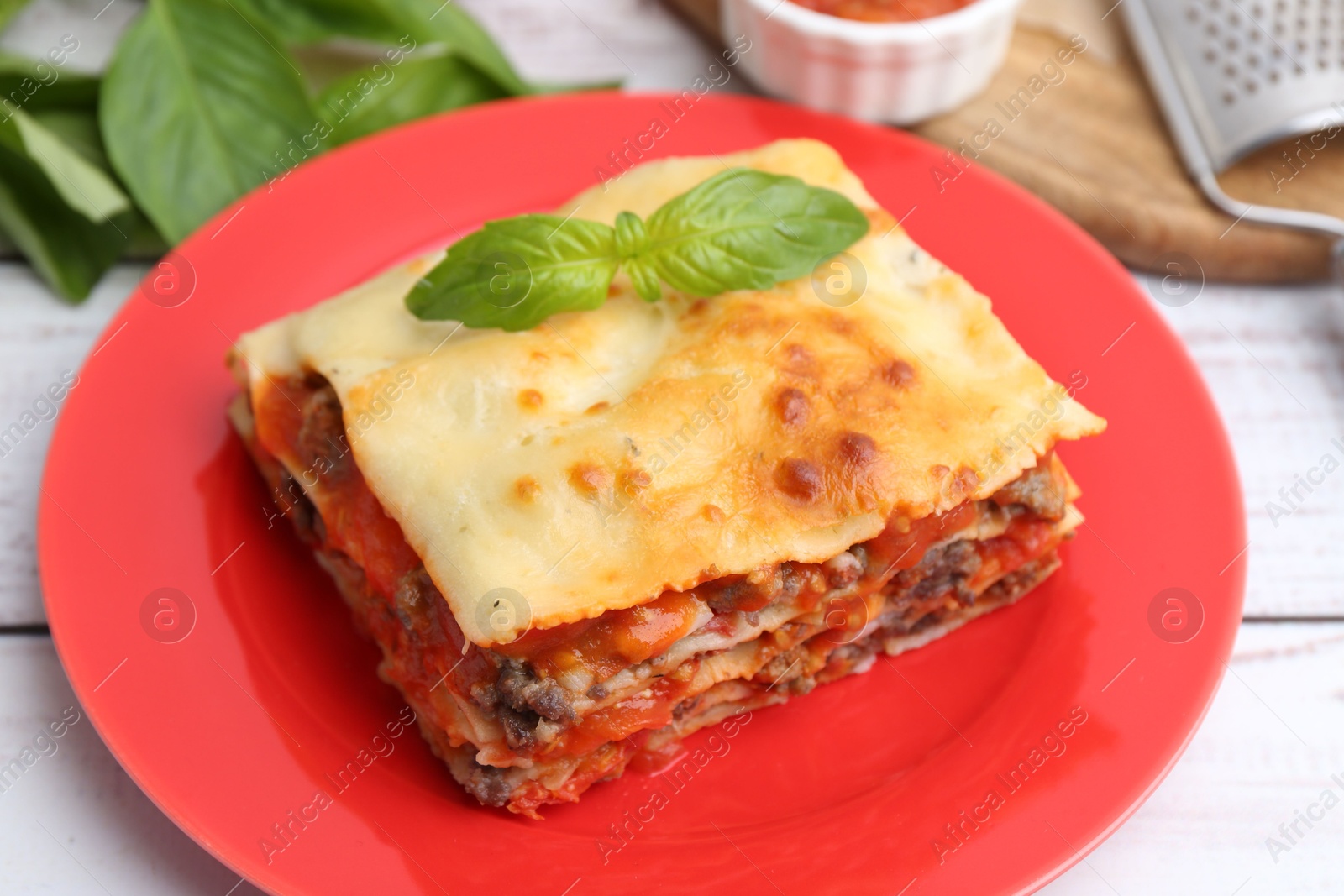 Photo of Piece of delicious cooked lasagna with basil on light wooden table, closeup