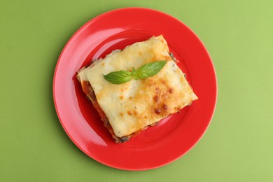 Photo of Piece of delicious cooked lasagna with basil on green background, top view