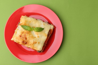 Photo of Piece of delicious cooked lasagna with basil on green background, top view. Space for text