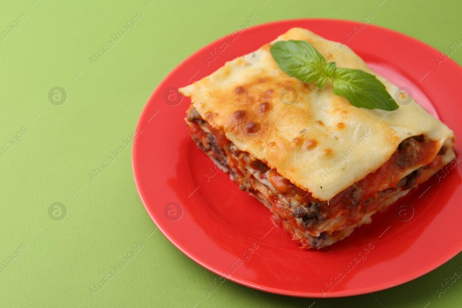 Photo of Piece of delicious cooked lasagna with basil on green background, closeup. Space for text