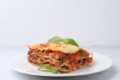 Photo of Piece of delicious cooked lasagna with basil on white table, closeup