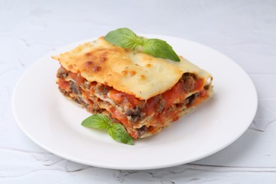 Photo of Piece of delicious cooked lasagna with basil on white textured table, closeup