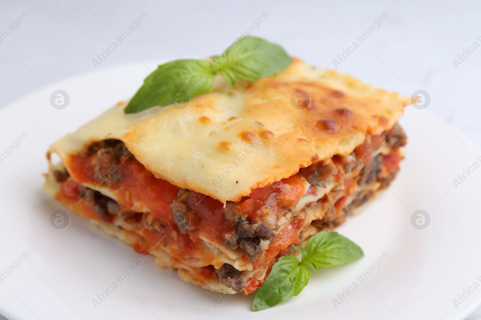 Photo of Piece of delicious cooked lasagna with basil on plate, closeup