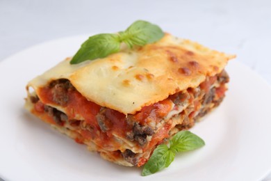 Piece of delicious cooked lasagna with basil on plate, closeup