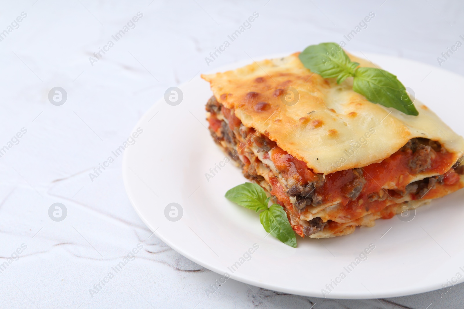 Photo of Piece of delicious cooked lasagna with basil on white textured table, closeup