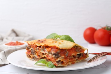 Photo of Piece of delicious cooked lasagna with basil on white table, closeup