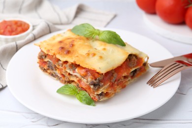 Photo of Piece of delicious cooked lasagna with basil on white textured table, closeup