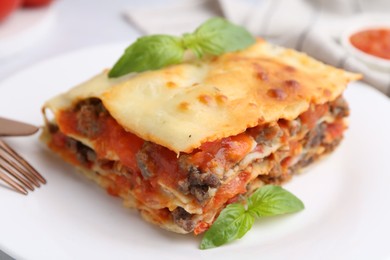 Photo of Piece of delicious cooked lasagna with basil on plate, closeup