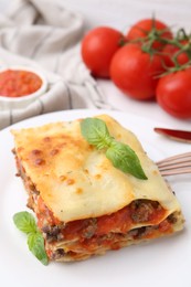 Photo of Piece of delicious cooked lasagna with basil on table, closeup