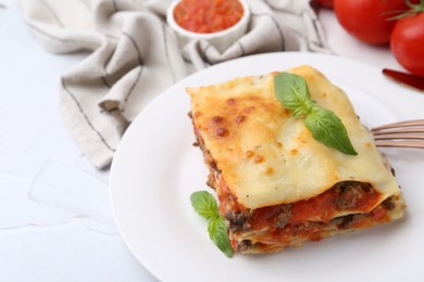 Photo of Piece of delicious cooked lasagna with basil on white textured table, closeup