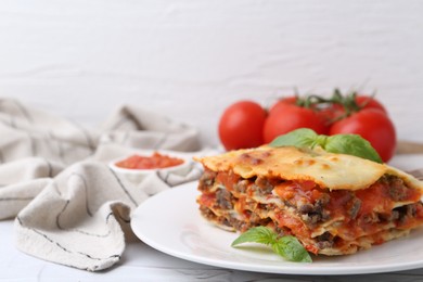 Photo of Piece of delicious cooked lasagna with basil on white textured table, closeup