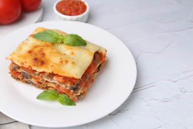 Photo of Piece of delicious cooked lasagna with basil on white textured table, closeup. Space for text