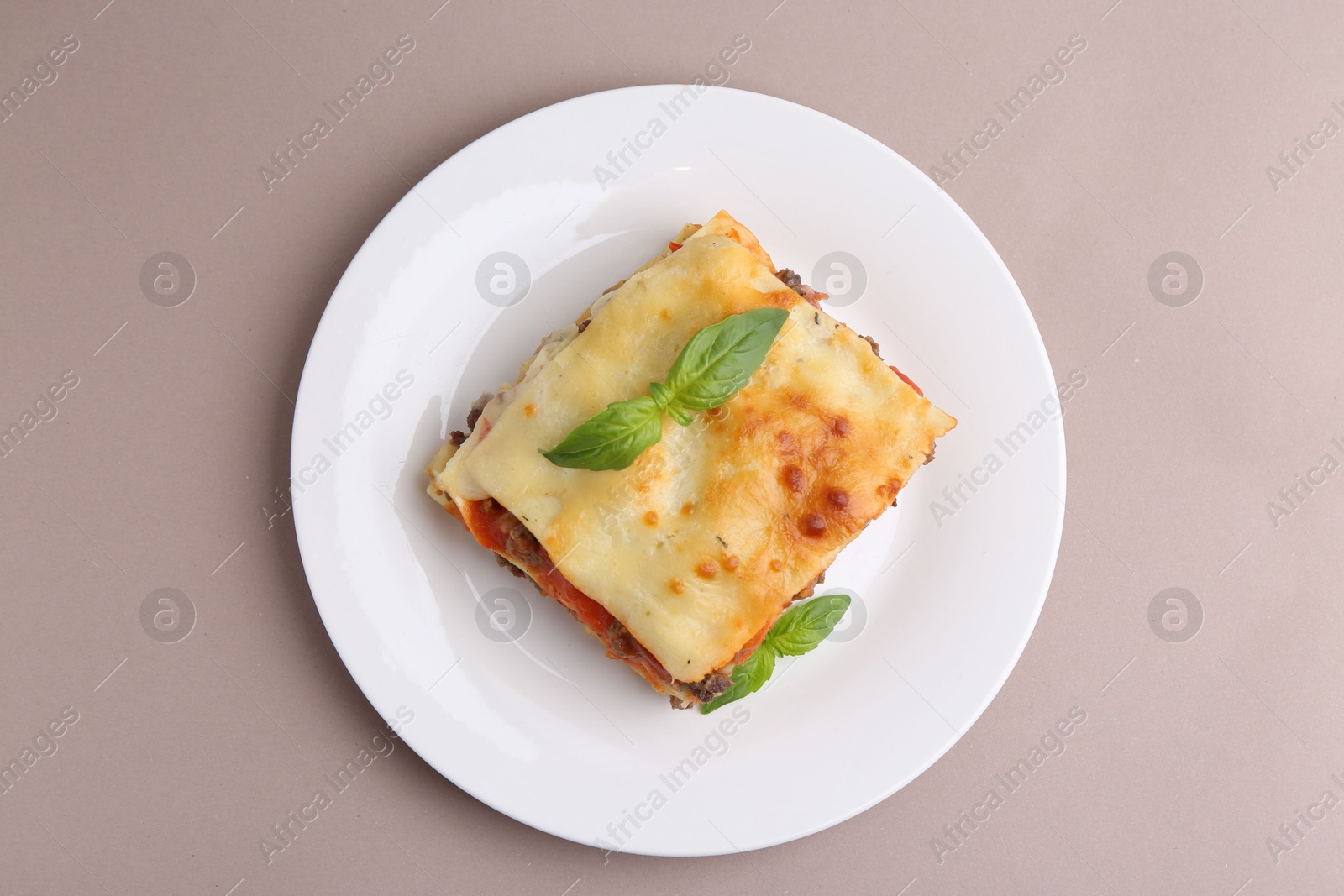 Photo of Piece of delicious cooked lasagna with basil on beige background, top view