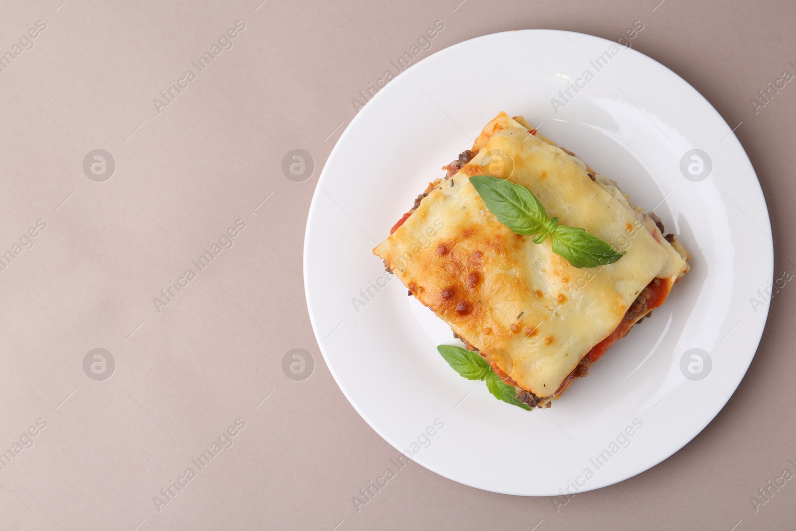 Photo of Piece of delicious cooked lasagna with basil on beige background, top view. Space for text