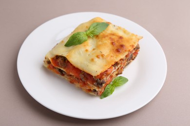 Photo of Piece of delicious cooked lasagna with basil on beige background, closeup