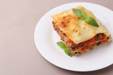 Photo of Piece of delicious cooked lasagna with basil on beige background, closeup. Space for text