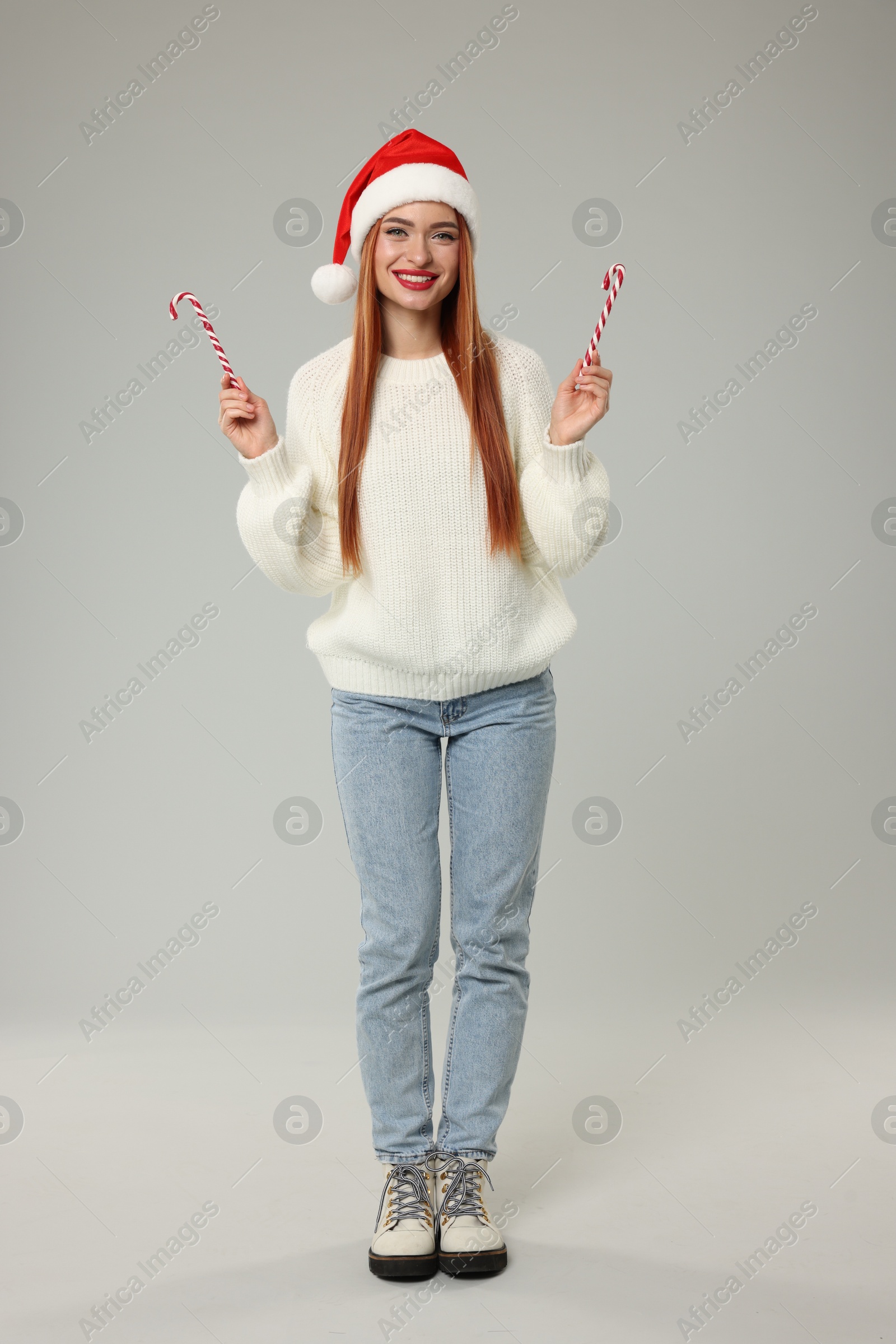 Photo of Young woman in Santa hat with candy canes on light grey background. Christmas celebration