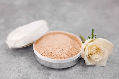 Photo of Face powder, puff applicator and rose flower on grey textured table, closeup