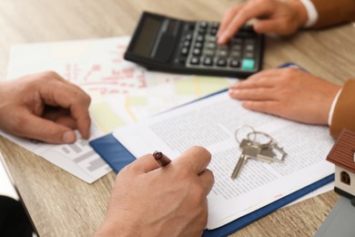 Photo of Real estate agent working with client at wooden table, closeup