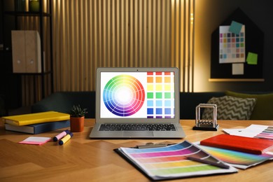 Photo of Designer's workplace with laptop, stationery and palettes on wooden table indoors