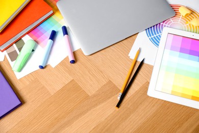 Photo of Designer's workplace with laptop, tablet, palettes and stationery on wooden table, above view