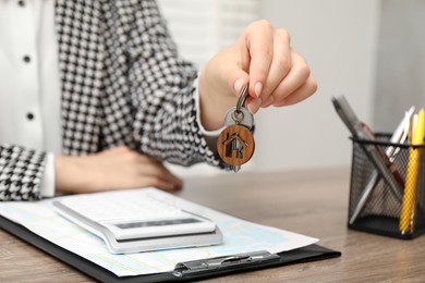 Photo of Real estate agent with house key at wooden table, closeup