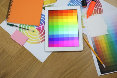 Photo of Designer's workplace with tablet, palettes and stationery on wooden table, flat lay