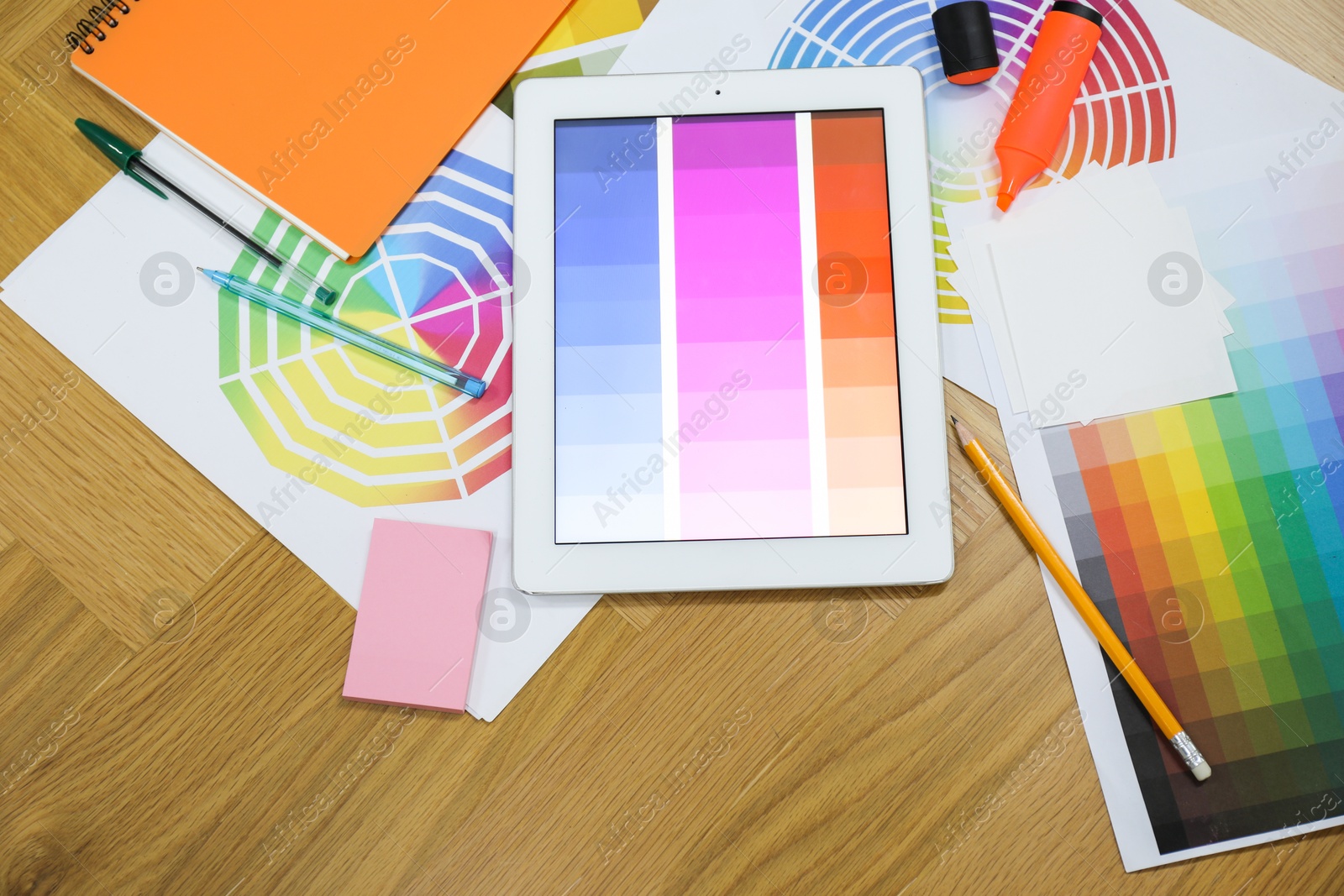 Photo of Designer's workplace with tablet, palettes and stationery on wooden table, flat lay