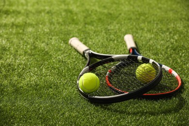 Photo of Tennis rackets and balls on green artificial grass, space for text