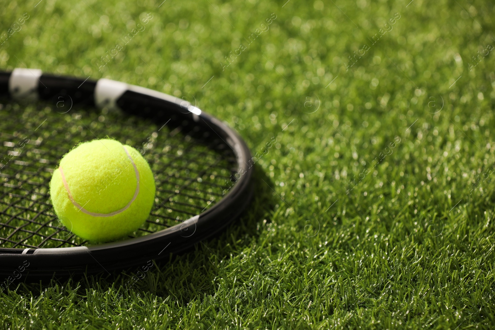 Photo of Tennis racket and ball on green artificial grass, closeup. Space for text